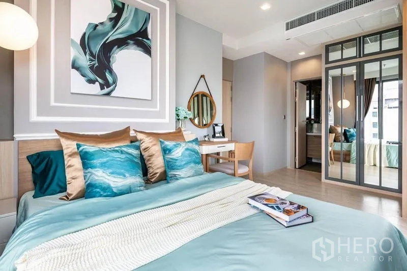 Condominium for rent or sale in Watthana, Bangkok - Primary bedroom with teal bedding, mirrored wardrobe and a compact study desk.