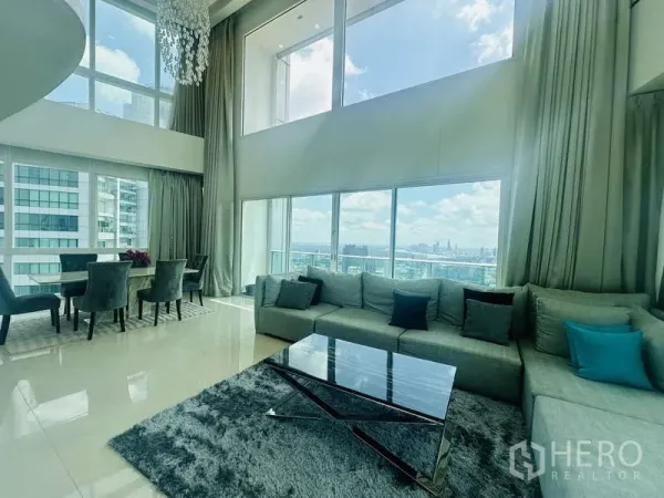 公寓 出租或出售在Khlong Toei, Bangkok - Millennium Residence 顶层复式客厅，挑高落地窗、沙发与餐区，远眺Benjakitti公园与曼谷天际线。
