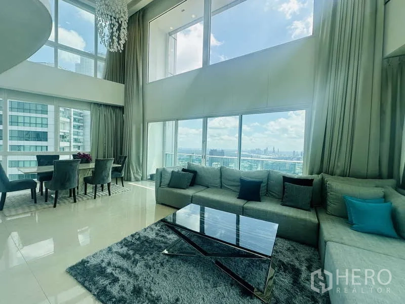 Condominium for rent or sale in Khlong Toei, Bangkok - Duplex penthouse living room at Millennium Residence with double-height ceiling, floor-to-ceiling windows, sofa set and dining area overlooking Benjakitti Park and Bangkok skyline.