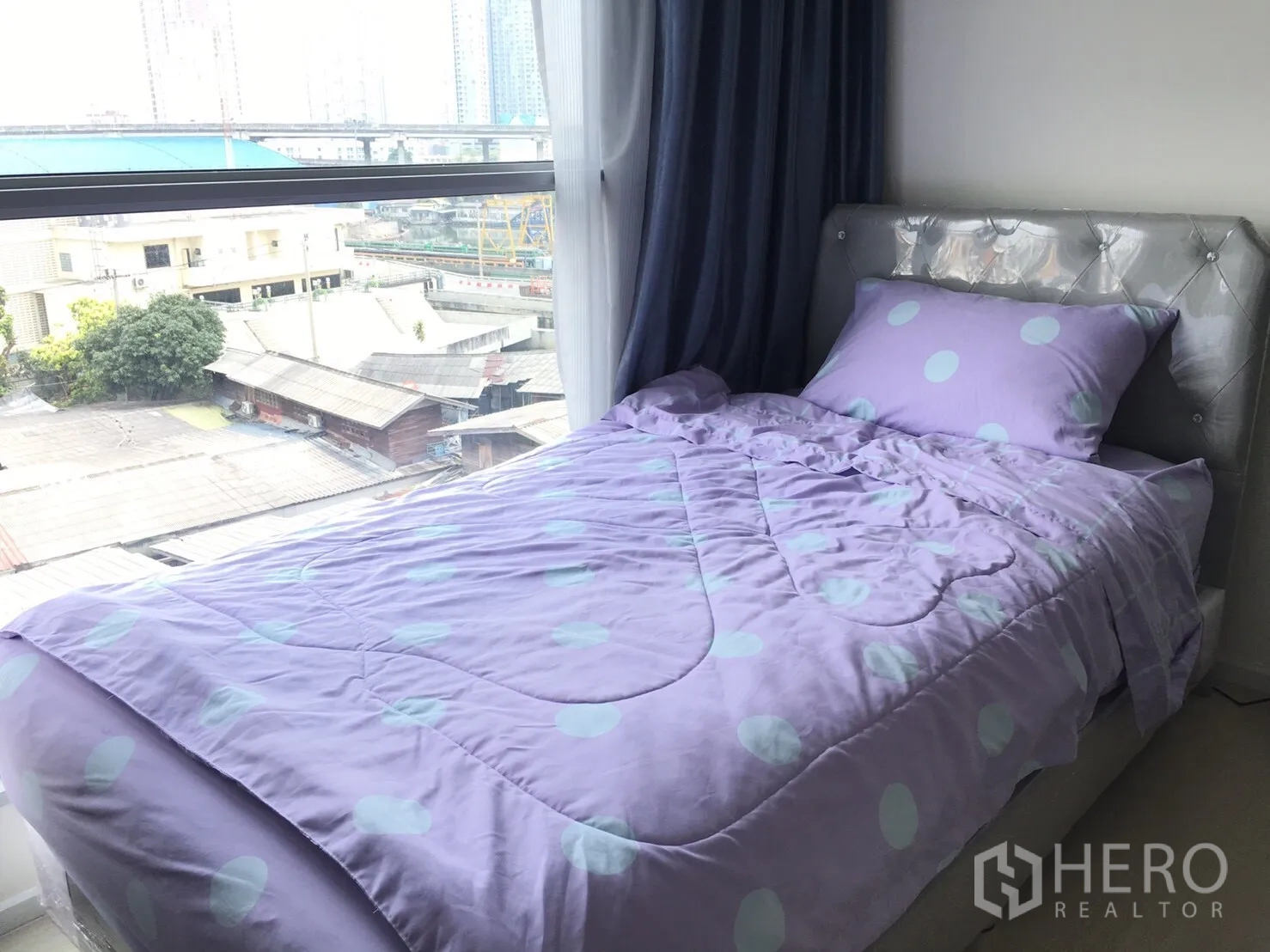 Condominium for rent in Khlong Toei, Bangkok - Cozy second bedroom with a single bed by a picture window overlooking city rooftops.