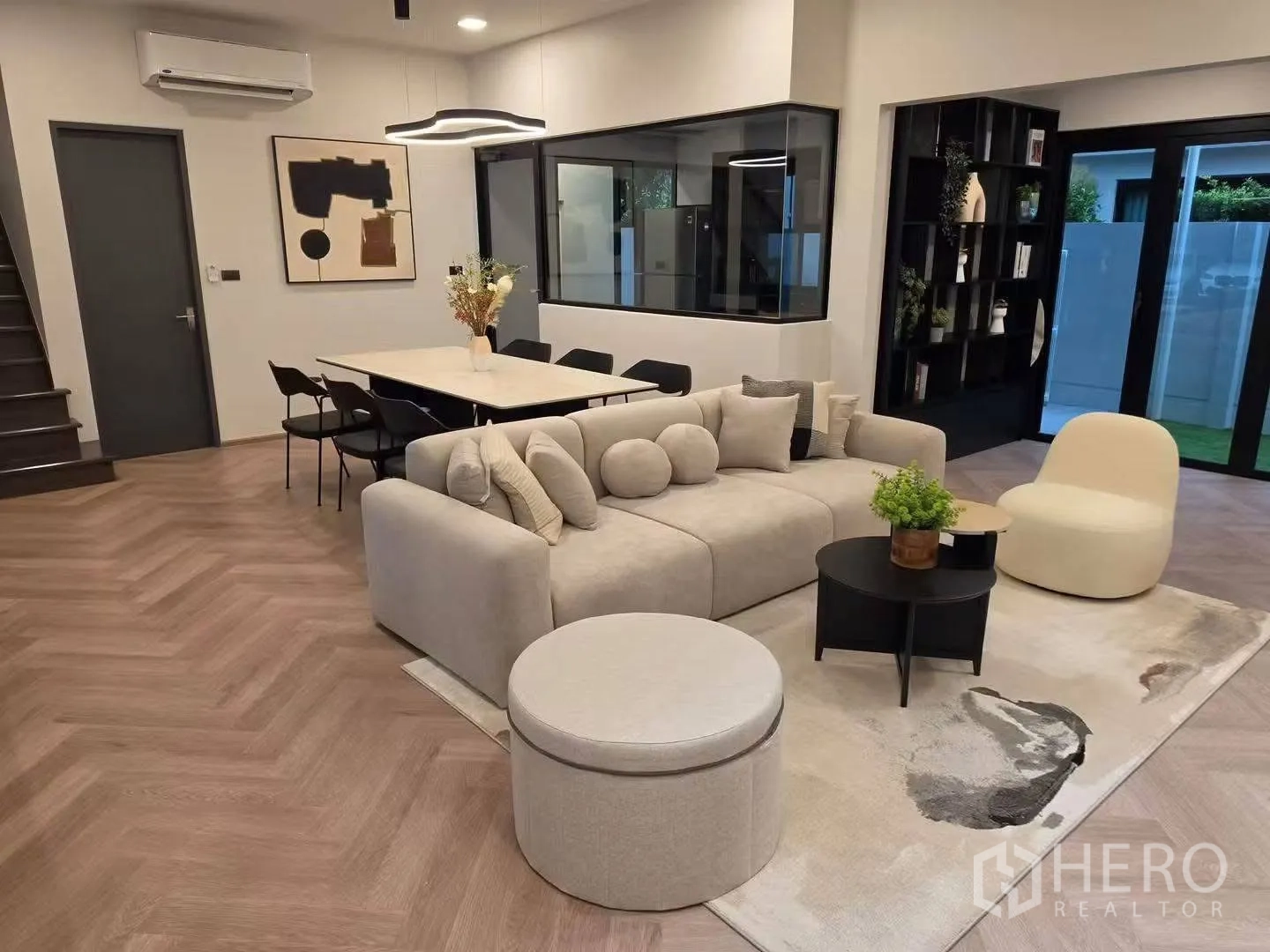 Townhouse for rent in Bang Phli, Samut Prakan - Cozy living room with sofa set, ottoman, dining table, artwork, and glass doors to a small garden.
