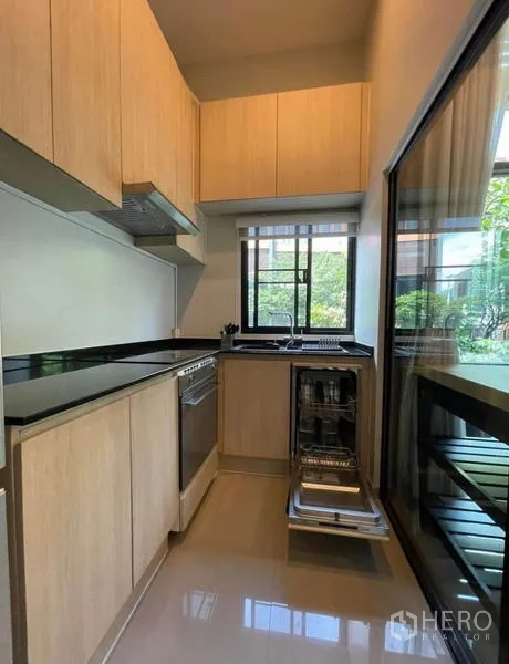 Townhouse for rent in Yan Nawa, Bangkok - Kitchen with dishwasher pulled out, black countertops, and window to garden.