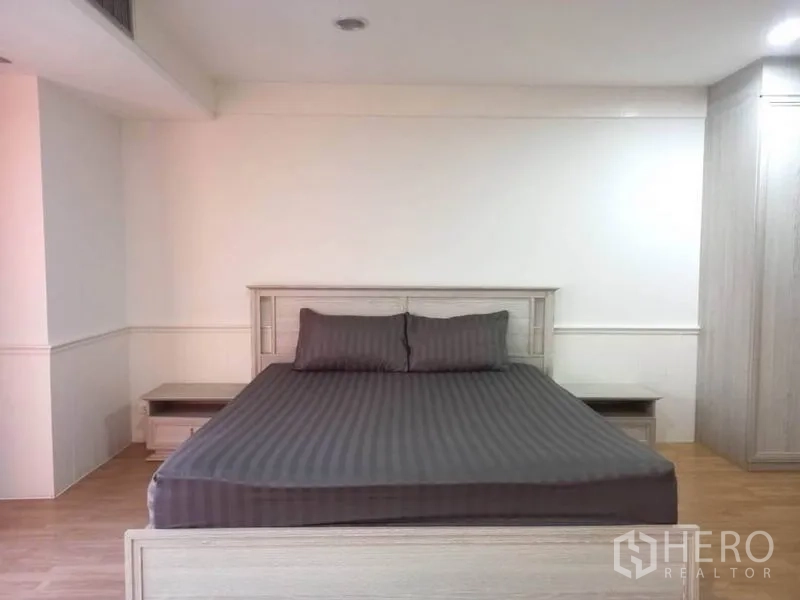 Condominium for rent in Khlong Toei, Bangkok - Spacious master bedroom with a king-size bed, bedside tables, and wood flooring.