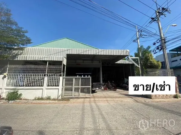 Warehouse for rent or sale in Mueang Samut Prakan, Samut Prakan - Front elevation of gated warehouse with wide driveway and perimeter fence on a quiet lane.