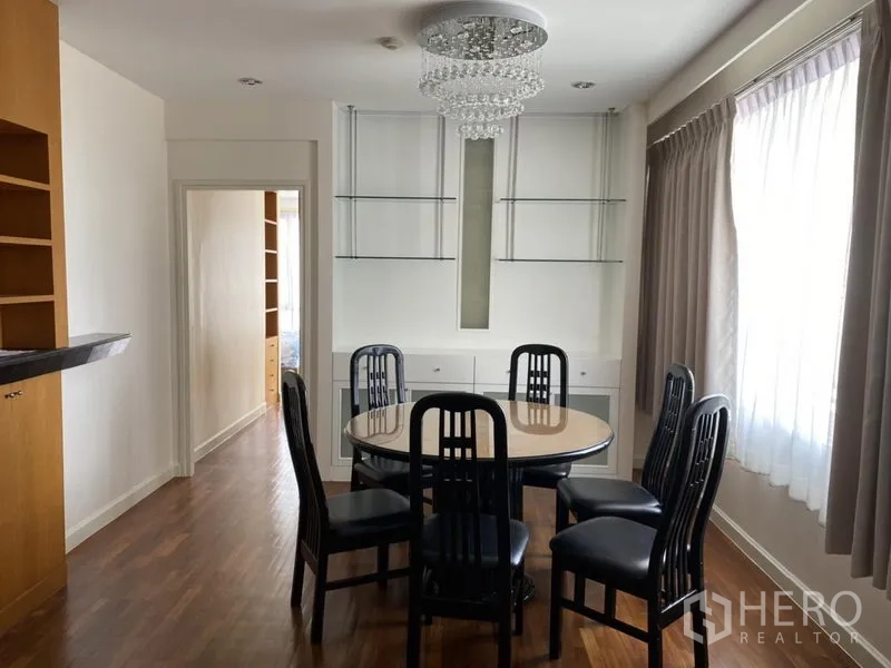 Condominium for rent or sale in Sathon, Bangkok - Windowed dining room featuring a round table for six, a crystal chandelier and display shelves.
