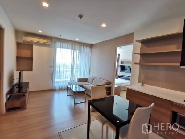 Condominium for rent or sale in Khlong Toei, Bangkok - Dining and lounge area with TV stand, full-height window to balcony, and open shelving.