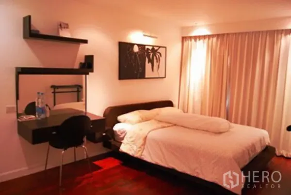 Condominium for rent in Pathum Wan, Bangkok - Cozy bedroom featuring a king bed, wall shelves, work vanity and full-length curtains with warm lighting.