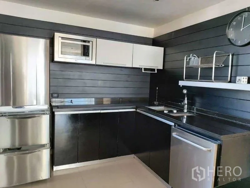 Condominium for rent in Watthana, Bangkok - U‑shaped kitchen close‑up with fridge, microwave, sink, and dark cabinetry.