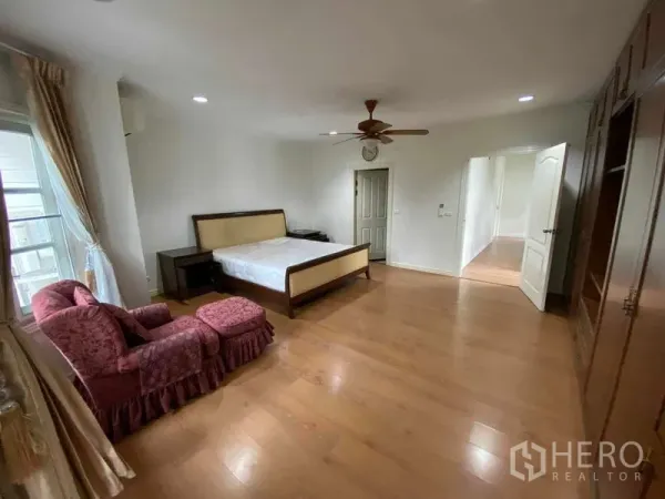 Townhouse for rent or sale in Mueang Samut Prakan, Samut Prakan - Master bedroom from another angle with armchair, built-in wardrobes and wooden floor.