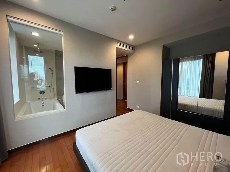 คอนโด ให้เช่า - ห้องนอนใหญ่ติดทีวี พร้อมช่องกระจกมองเข้าไปยังห้องน้ำในตัวที่มีอ่างอาบน้ำ