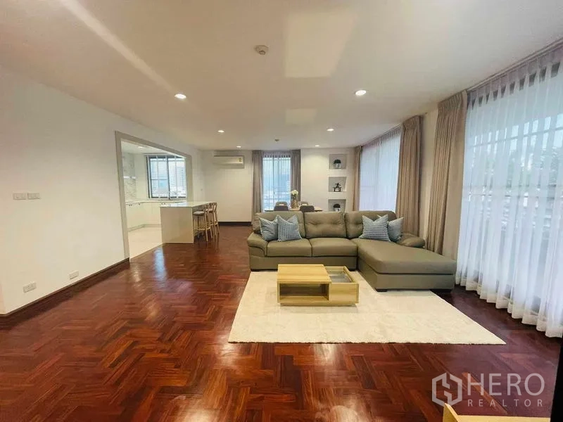 Condominium for rent - Large living room with L-shaped sofa, recessed lights, and full-height curtains.