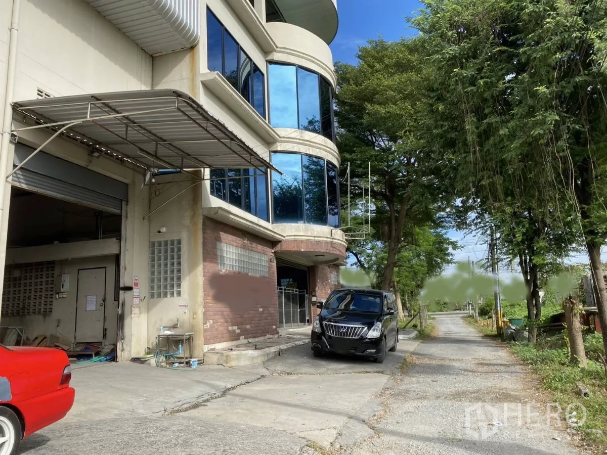 Warehouse for rent or sale in Mueang Nonthaburi, Nonthaburi - Loading bay with roller shutter door, canopy and on-site parking beside trees.