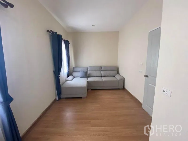 Townhouse for sale in Saphan Sung, Bangkok - Upstairs multipurpose room with an L-shaped sofa, windows and wood flooring.
