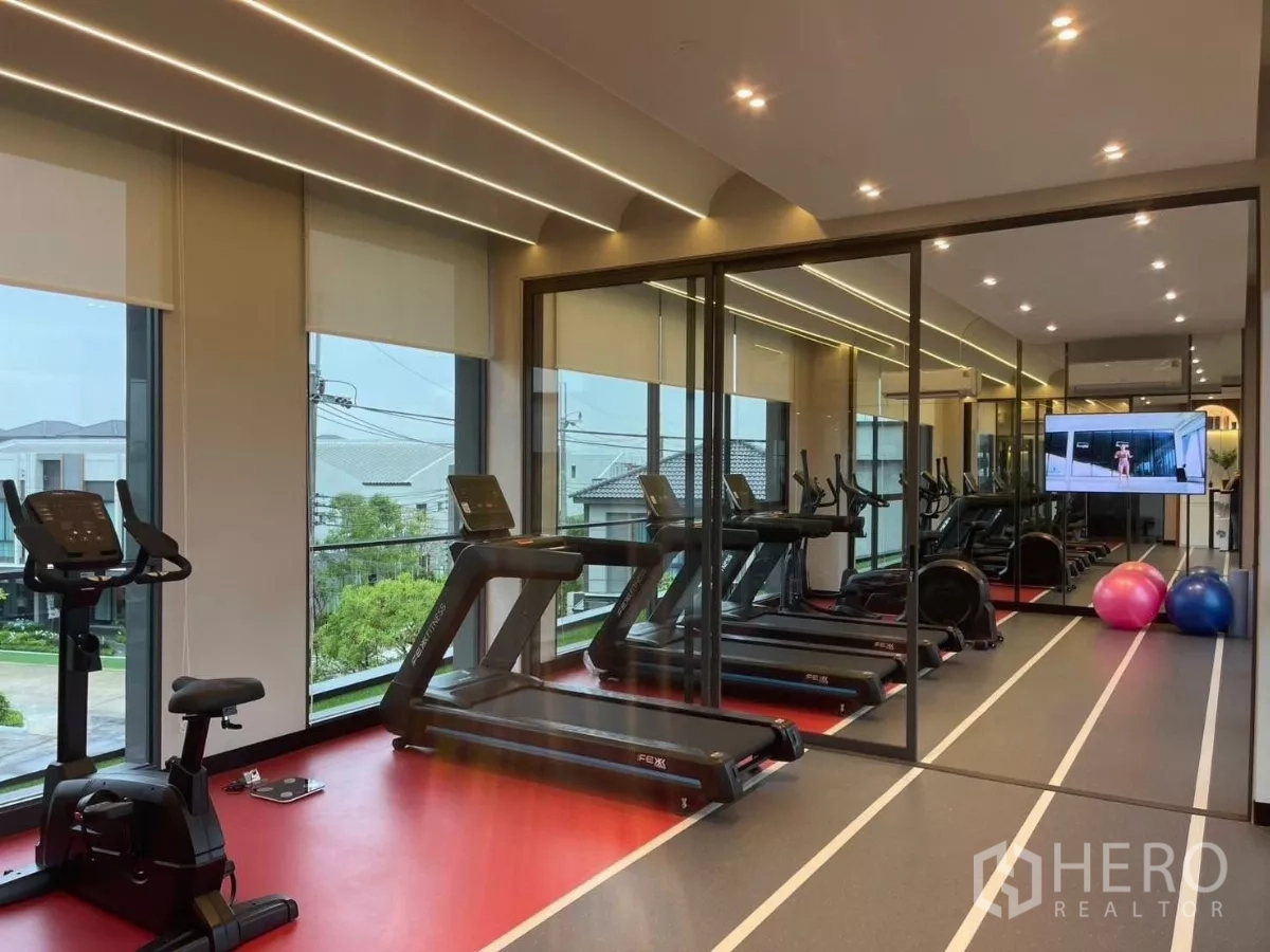 Townhouse for rent in Samut Prakan - Glass-walled fitness room featuring treadmills, bikes and a mirrored wall.