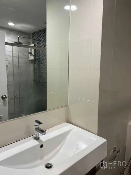 公寓 出售在Bang Na, Bangkok - 浴室洗手台与大镜面，背景可见玻璃淋浴间。