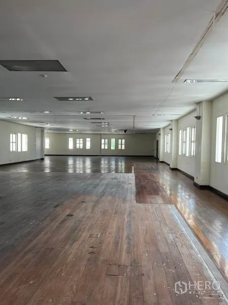 办公空间 出租在Khlong Toei, Bangkok - 长形办公大厅，混色木地板、多扇窗户与吊顶灯带贯穿空间。