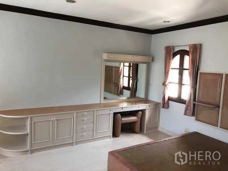 Detached House for rent in Phra Khanong, Bangkok - Spacious bedroom with built‑in dressing table, mirror and arched window.