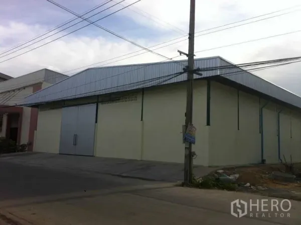 Warehouse for rent in Bang Phli, Samut Prakan - Street-facing exterior of a Bang Phli warehouse with corrugated metal roof and a large steel sliding door.