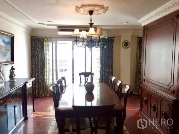 Condominium for rent or sale in Pathum Wan, Bangkok - Formal dining room with chandelier, long wooden table and sliding doors to a bright balcony in a Pathum Wan condominium.