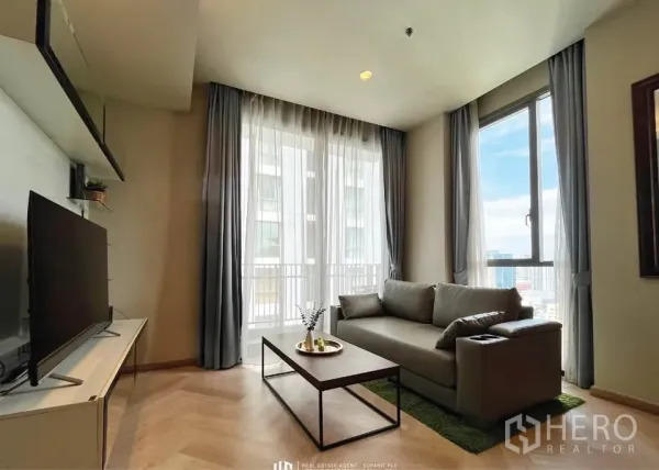 Condominium for rent in Watthana, Bangkok - Corner living area with floor-to-ceiling windows, city view, gray sofa and TV console.