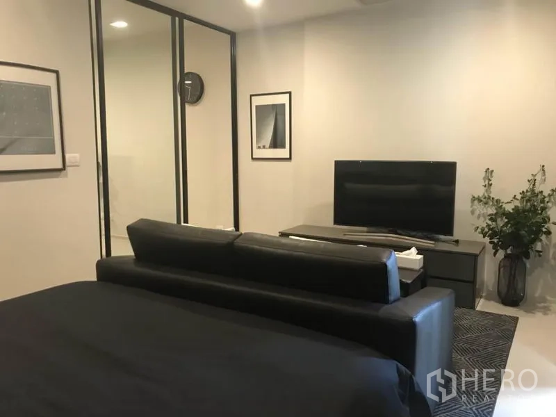 公寓 出租或出售在Pathum Wan, Bangkok - 卧室与起居一体，黑色沙发对着电视柜，玻璃隔断墙