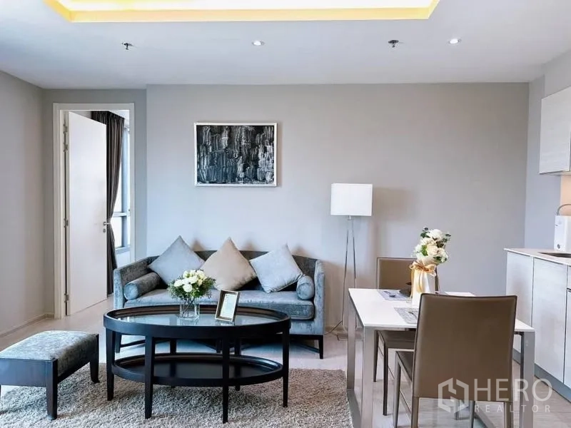 Condominium for rent in Watthana, Bangkok - Living area with sofa, oval coffee table and dining for two beside the kitchen.