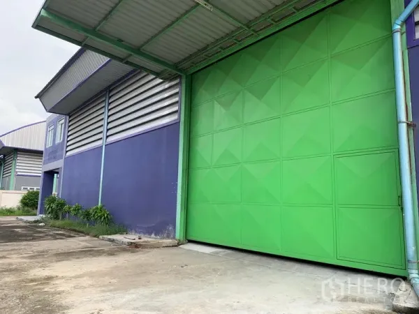 คลังสินค้า ให้เช่าในLam Luk Ka, Pathum Thani - ประตูสไลด์สีเขียวขนาดใหญ่พร้อมกันสาดและลานคอนกรีตกว้างข้างอาคารโกดัง