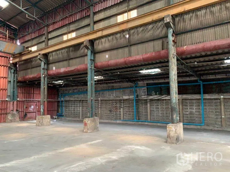 Warehouse for rent in Bang Kho Laem, Bangkok - Side bay with steel posts, overhead beams and visible blue utility piping.
