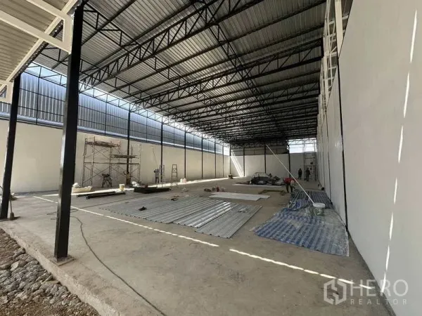 Warehouse for rent in Lam Luk Ka, Pathum Thani - Side perspective of the warehouse interior showing open floor, steel roof structure and materials on the ground