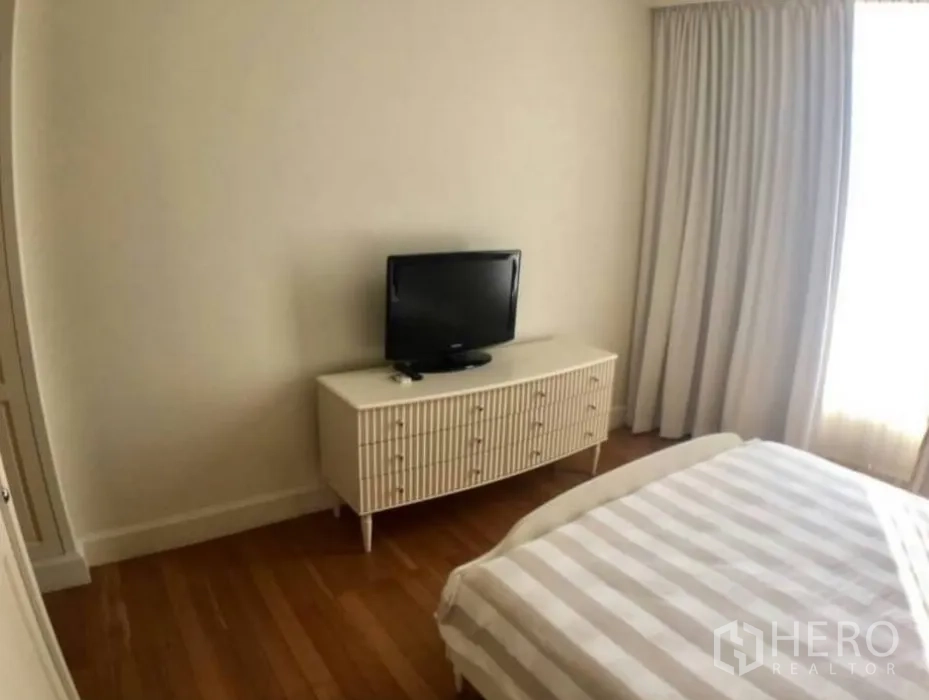 Condominium for rent in Watthana, Bangkok - Cozy bedroom with TV console, full-length curtains and warm wooden flooring.