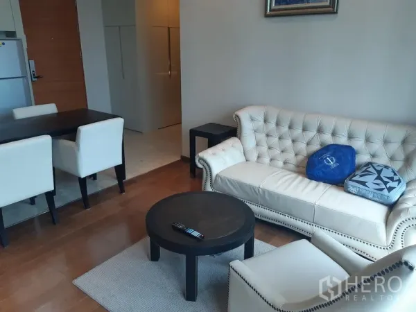 Condominium for rent in Khlong Toei, Bangkok - Bright living room with tufted cream sofa, armchair and round coffee table beside the dining area.