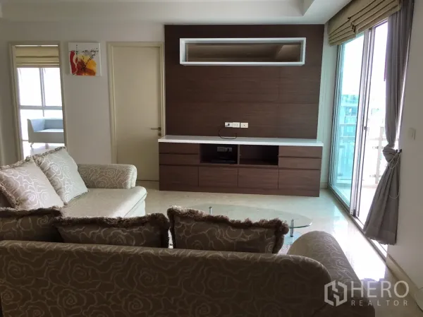 Condominium for rent or sale in Khlong Toei, Bangkok - Bright living room with patterned sofa, wood media wall and sliding doors to a balcony.