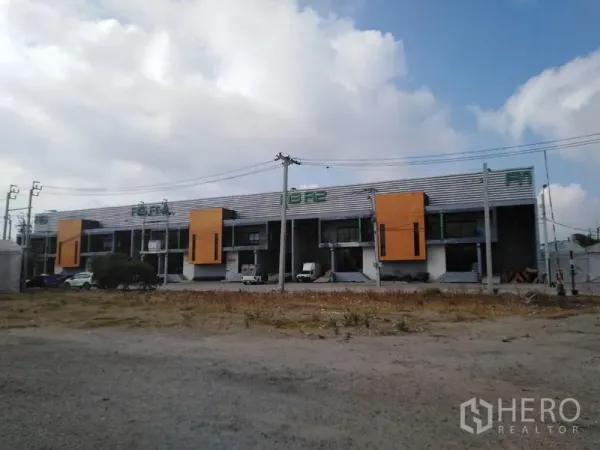 Factory for rent in Samut Prakan - Panoramic exterior of multiple warehouse bays with parking and power lines on a clear day.