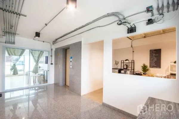 Home Office for rent in Phaya Thai, Bangkok - Bright lobby with elevator, exposed conduits and glass door opening to a meeting area.