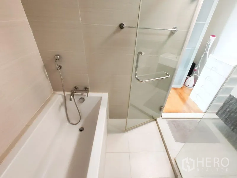 Condominium for rent in Khlong Toei, Bangkok - Close-up of bathtub and frameless glass shower door with handheld shower.