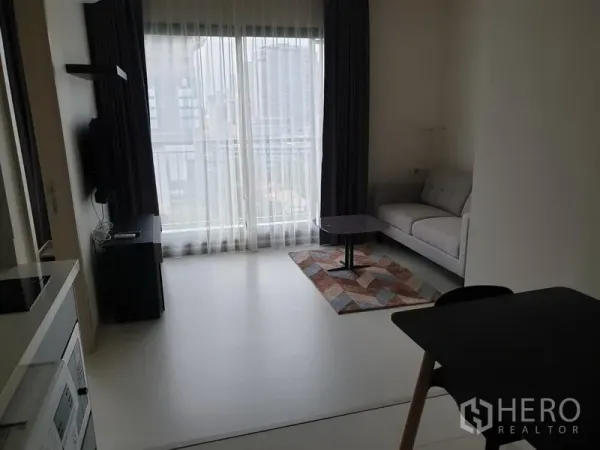 公寓 出租在Khlong Toei, Bangkok - 明亮客厅，落地窗与纱帘、灰色沙发和小茶几，可见城市景观，位于空堤区通罗站附近的公寓。