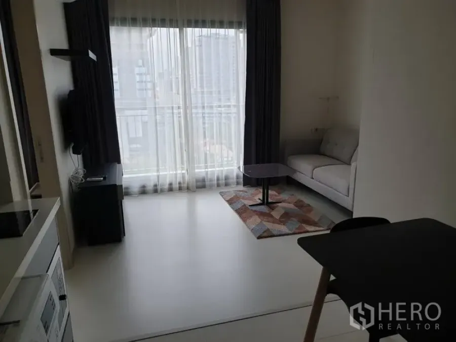 公寓 出租在Khlong Toei, Bangkok - 明亮客厅，落地窗与纱帘、灰色沙发和小茶几，可见城市景观，位于空堤区通罗站附近的公寓。
