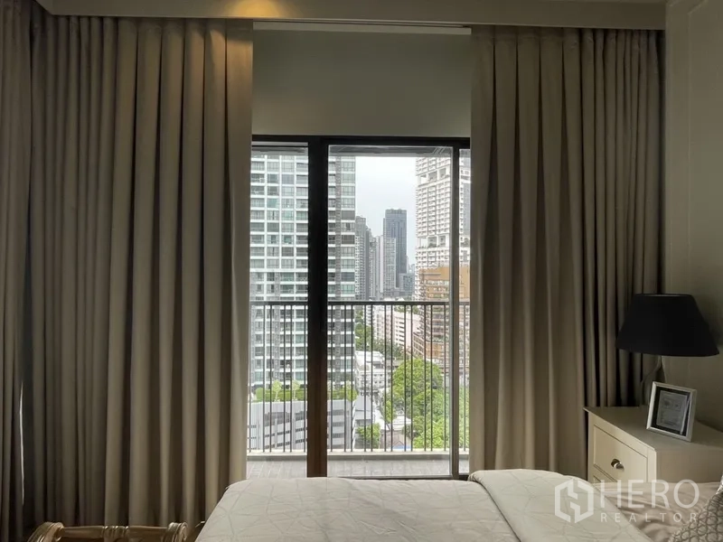 คอนโด ให้เช่าในBangkok - ห้องนอนมีผ้าม่านเต็มบานและระเบียงมองเห็นสกายไลน์กรุงเทพฯ