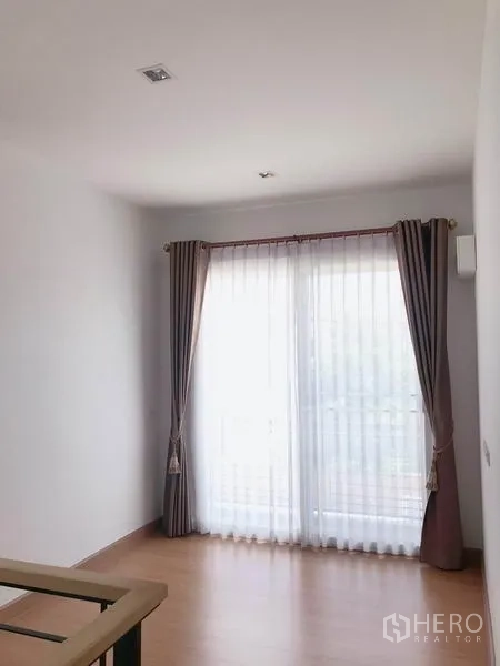 Detached House for sale in Suan Luang, Bangkok - Sunlit room with sliding glass doors to a balcony and floor-length curtains.