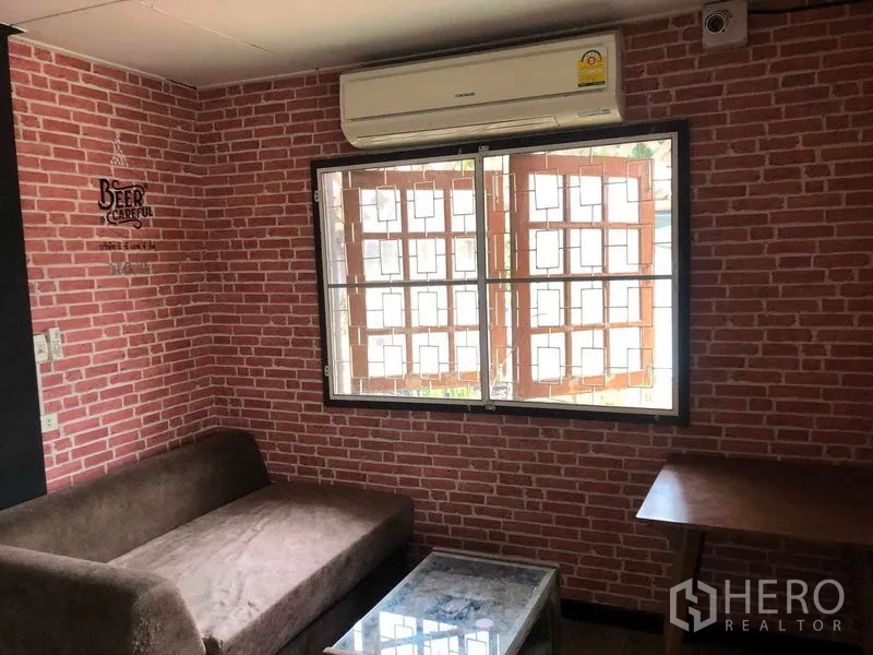 Detached House for sale in Wang Thonglang, Bangkok - Cozy room featuring brick-pattern walls, a window with security grilles, a sofa and an air conditioner.
