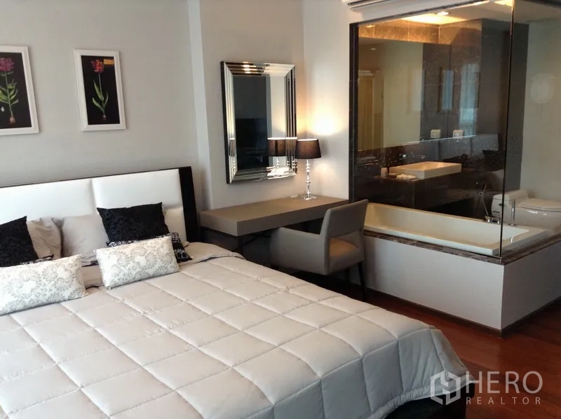 公寓 出租在Watthana, Bangkok - 主卧带软包床头、工作台，玻璃隔断浴室内设浴缸与盥洗台。