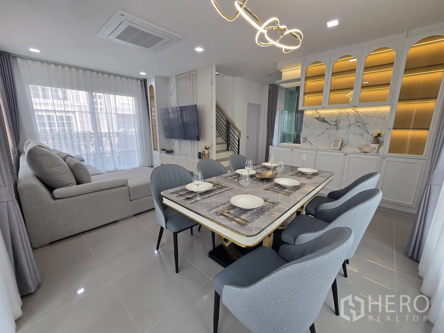 Semi-detached House for rent in Mueang Samut Prakan, Samut Prakan - Dining zone facing TV wall and staircase, with illuminated display cabinets and marble backsplash.