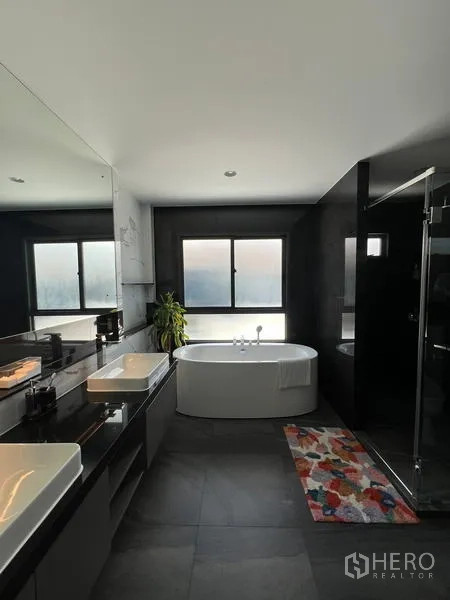 Detached House for rent in Bang Kapi, Bangkok - Luxury bathroom with freestanding bathtub, double vanity and glass-enclosed shower beside frosted windows.