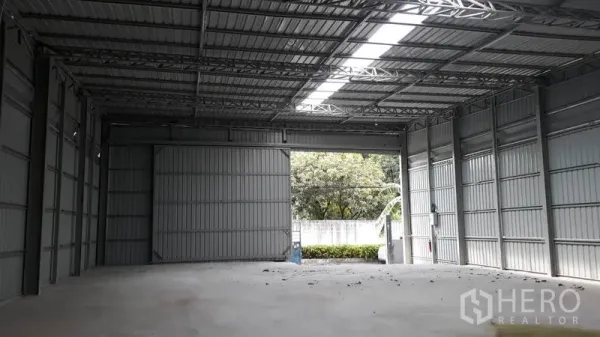 Warehouse for rent in Lat Phrao, Bangkok - Spacious steel-frame warehouse interior with high ceiling, concrete floor, skylight strip and large sliding doors opening to the yard in Lat Phrao, Bangkok.