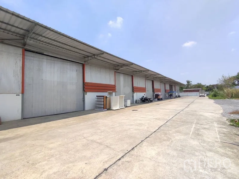 Warehouse for rent in Pathum Thani - Row of warehouses with large roller shutter doors, covered loading bays and a wide concrete yard.
