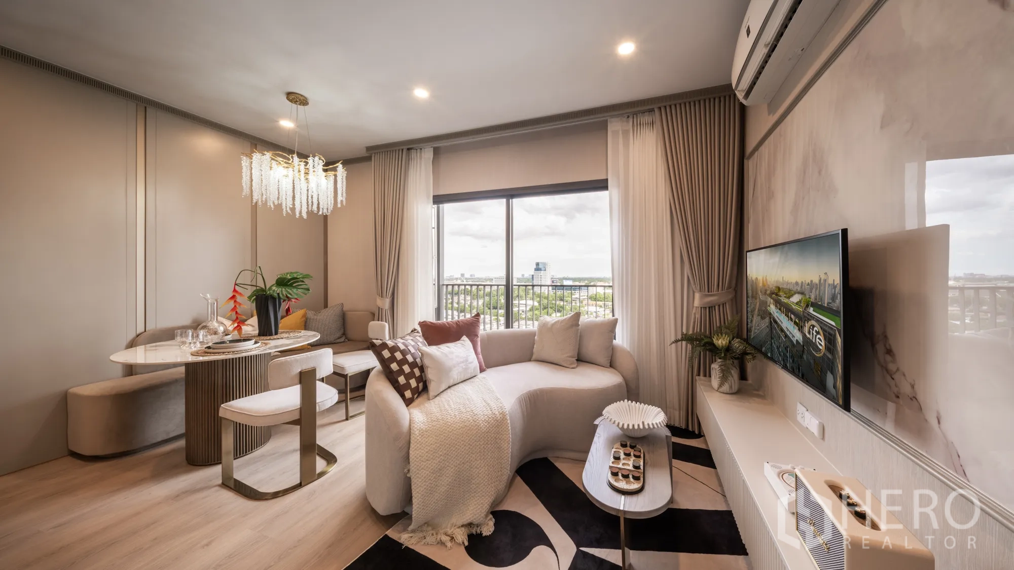 Condominium for sale in Khlong Toei, Bangkok - Bright living and dining area with curved sofa, chandelier, TV wall, and large window with city view.