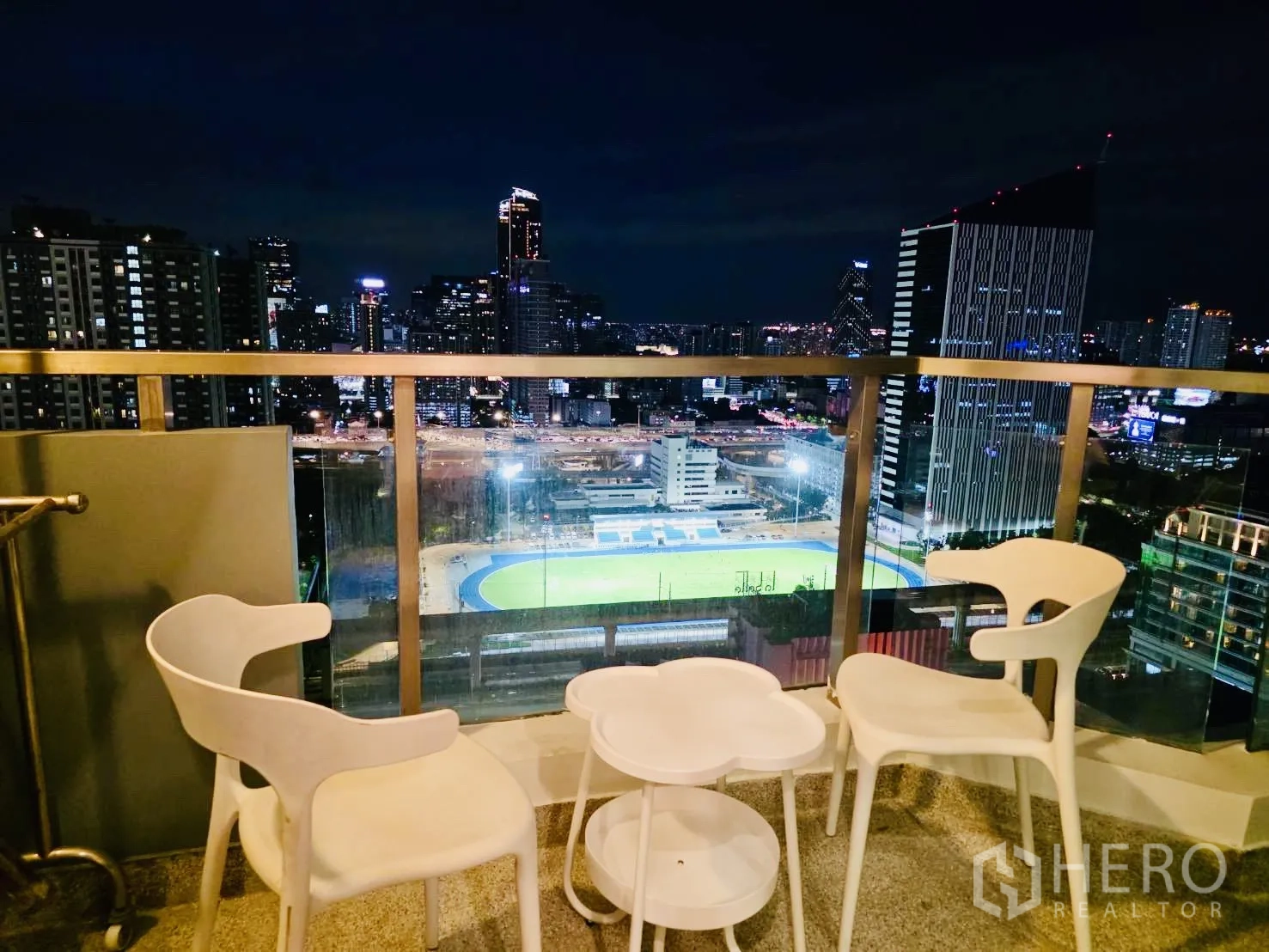 คอนโด for rent in Huai Khwang, Bangkok - วิวกลางคืนจากระเบียงพร้อมชุดเก้าอี้ มองเห็นแสงไฟเมืองและสนามกีฬา