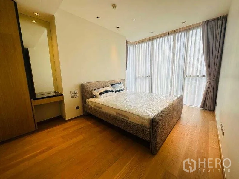 Condominium for rent in Khlong Toei, Bangkok - Spacious master bedroom with large windows, sheer curtains, and a built-in vanity.