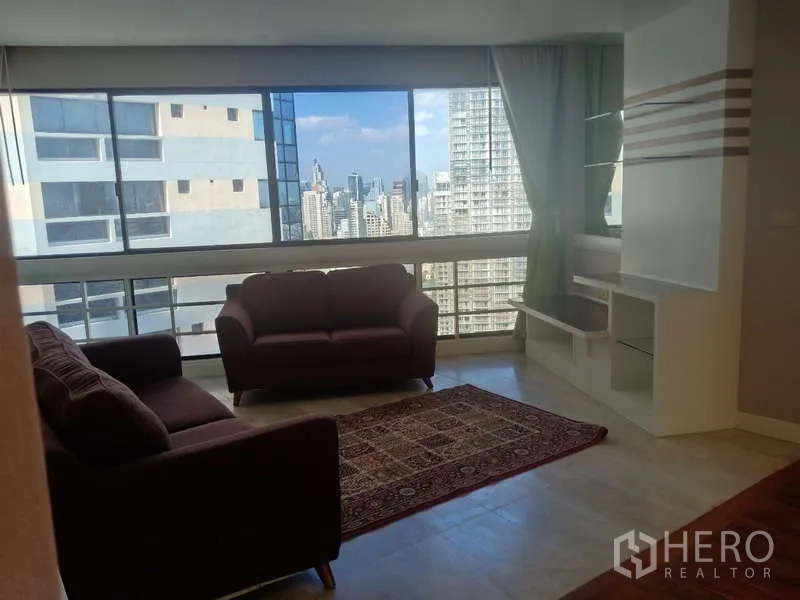 Condominium for rent in Khlong Toei, Bangkok - Sitting area with two sofas, rug and panoramic city skyline through wide windows.