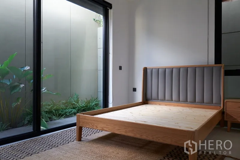 Detached House for rent in Watthana, Bangkok - Ground-floor bedroom with wooden bedframe and garden access through sliding doors.